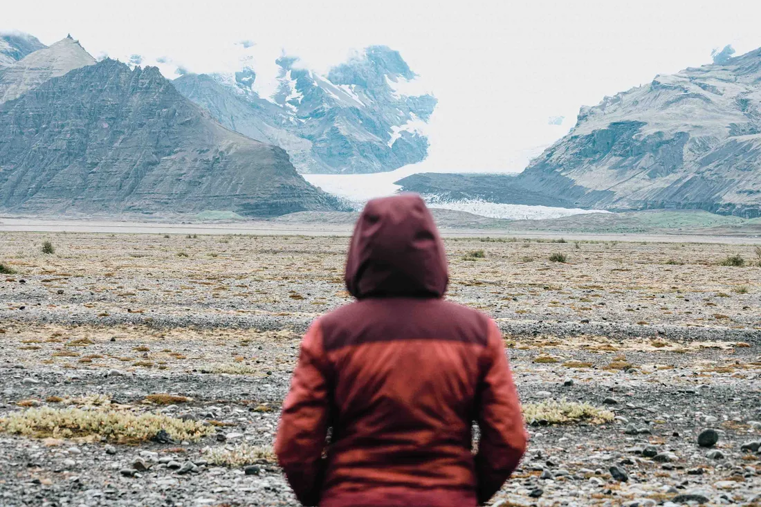 Person in roter Jacke blickt auf eine weite Berglandschaft mit Gletscher