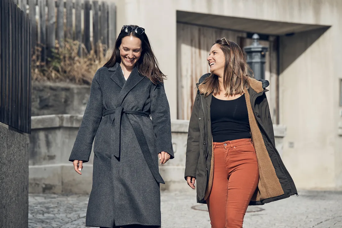 Due donne camminano sorridendo per una strada in città.