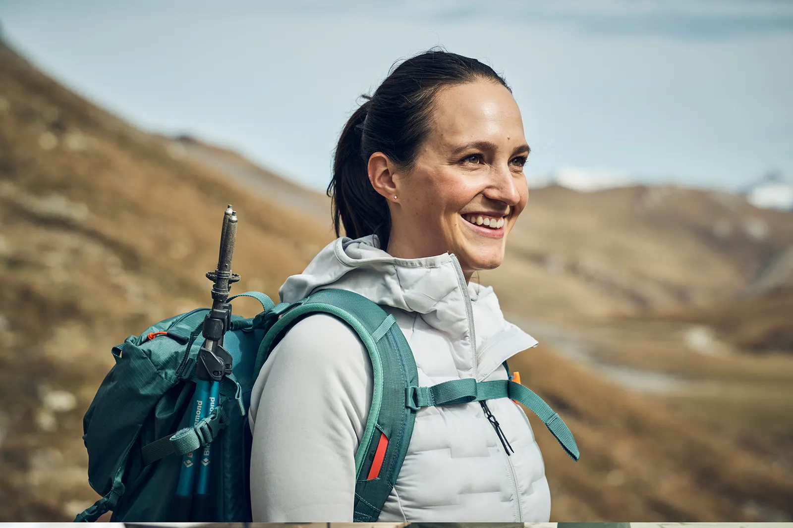 Una donna con uno zaino si trova in un paesaggio di montagna e sorride.