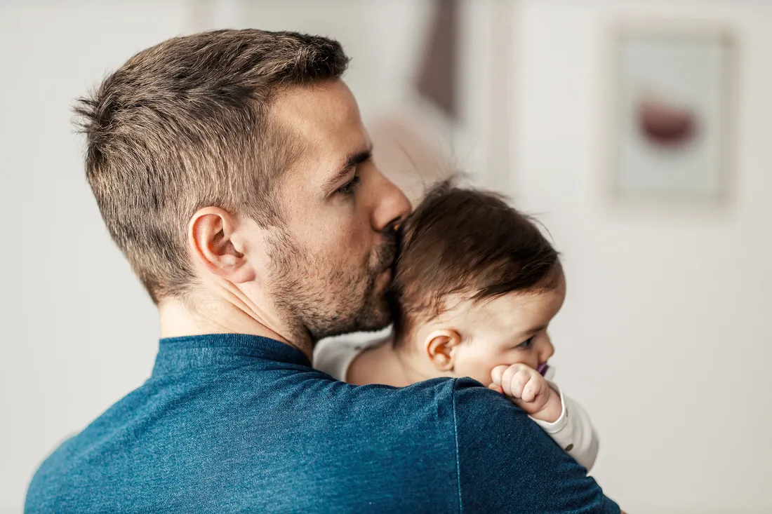 Un padre tiene in braccio il suo bambino e gli bacia la testa.