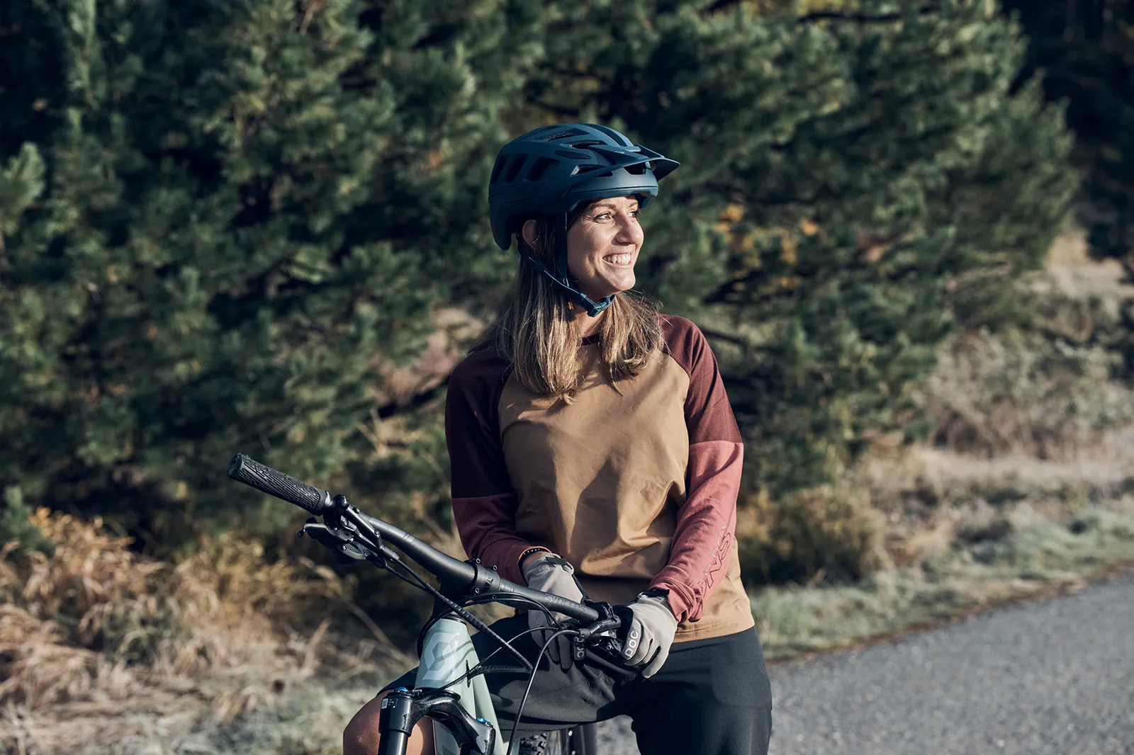 Una donna con casco tiene una mountain bike su un sentiero nella natura.