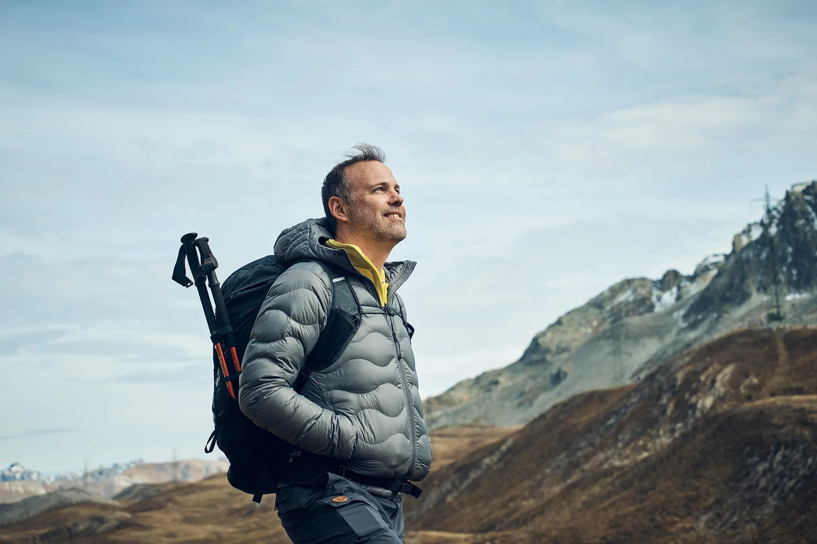 Un uomo con uno zaino si trova in un paesaggio di montagna e guarda in lontananza.