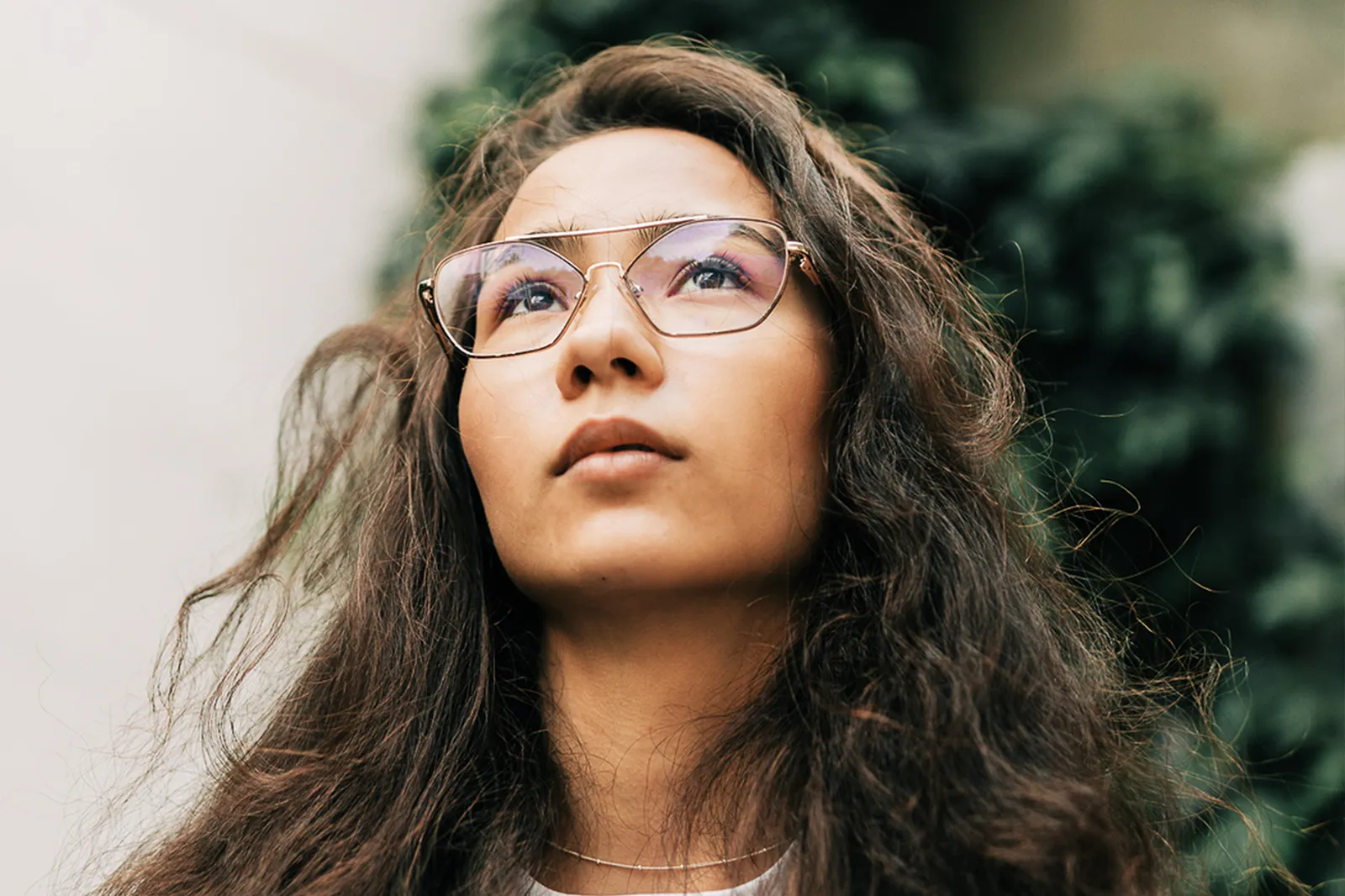Una donna con gli occhiali guarda verso l’alto all’aperto.