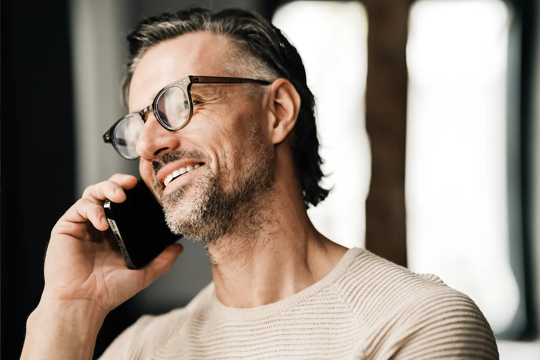 Un uomo con gli occhiali parla al telefono sorridendo.