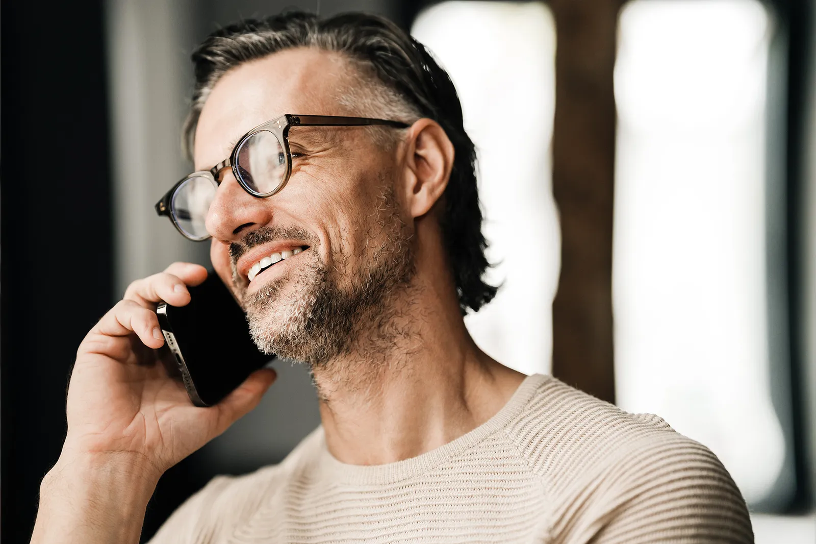 Un uomo con gli occhiali parla al telefono sorridendo.