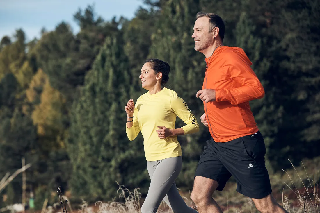 Una donna e un uomo fanno jogging su un sentiero nella natura davanti a un bosco.
