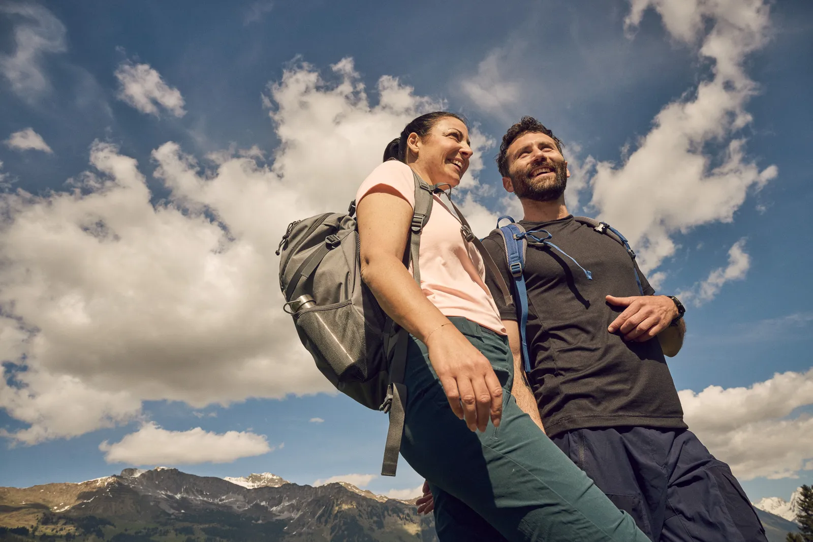 Due persone fanno un'escursione con lo zaino ammirando il panorama delle montagne circostanti.