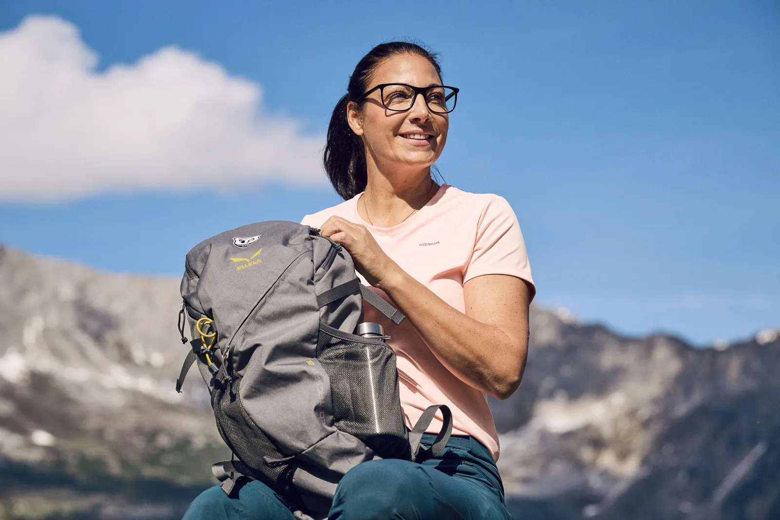 Una persona con uno zaino si riposa in montagna davanti a un paesaggio alpino.