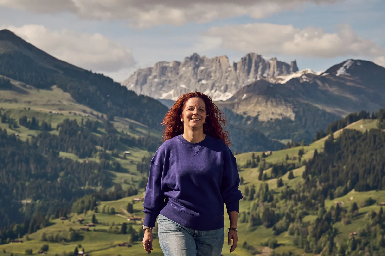 Una persona cammina in un paesaggio alpino con montagne sullo sfondo.