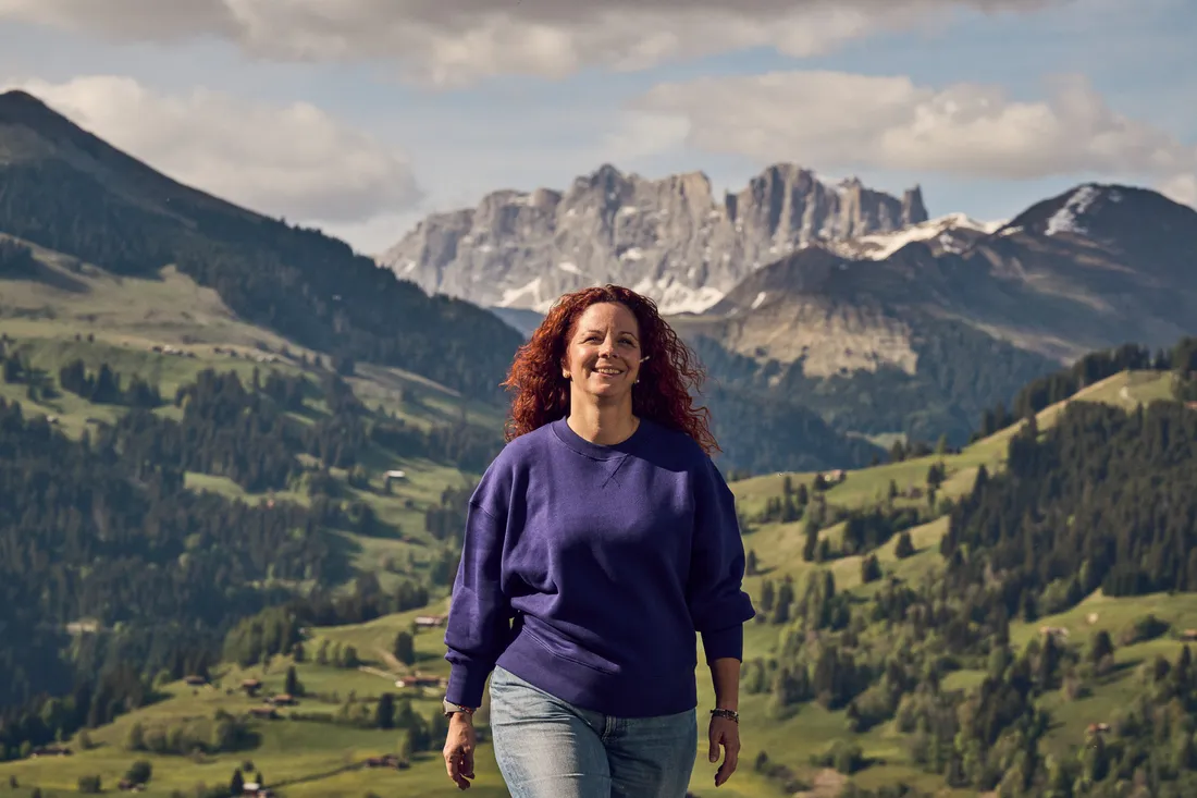 Eine Person geht durch eine alpine Landschaft mit Bergen im Hintergrund.