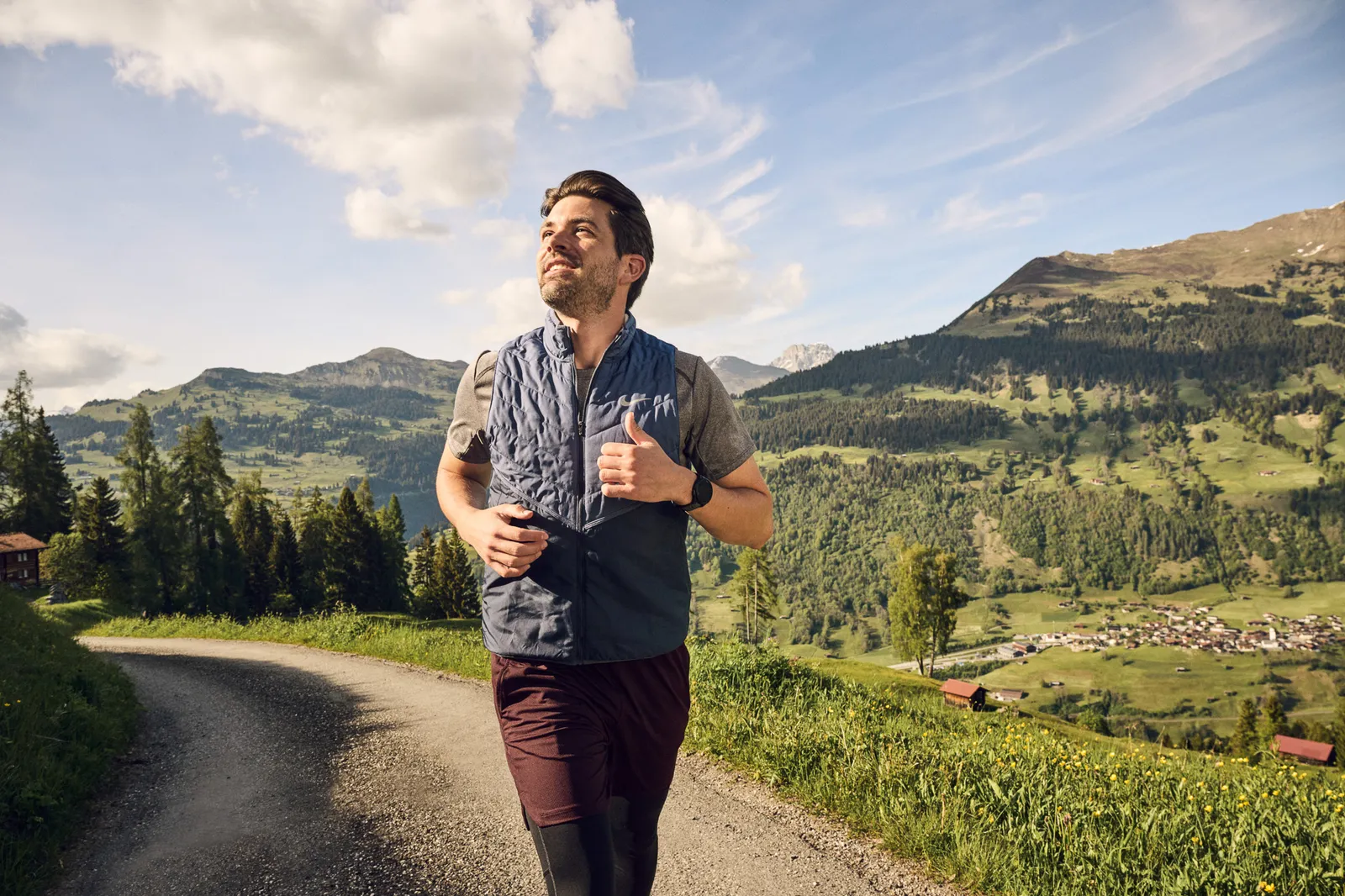 Una persona corre su un sentiero immerso in un paesaggio alpino con montagne sullo sfondo.
