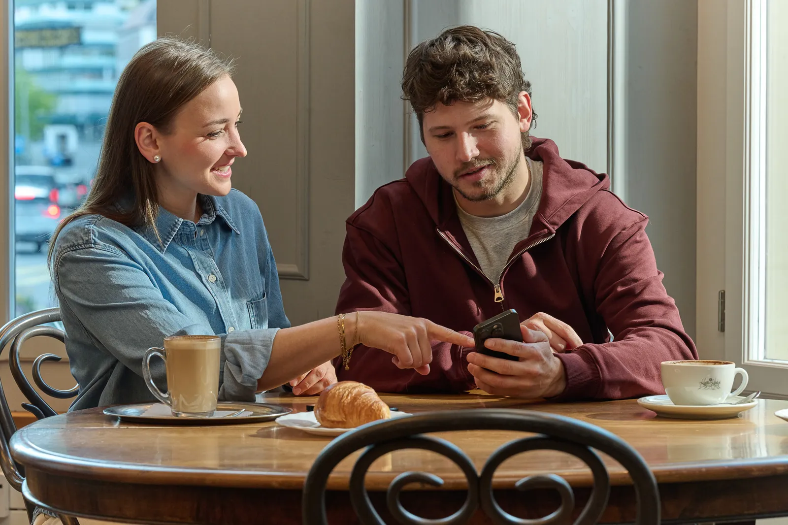 Due persone sono sedute allo stesso tavolo in un caffè e osservano insieme uno smartphone.