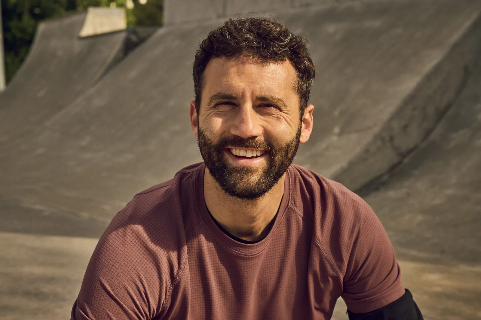 Eine Person sitzt in einem Skatepark und blickt in die Kamera.