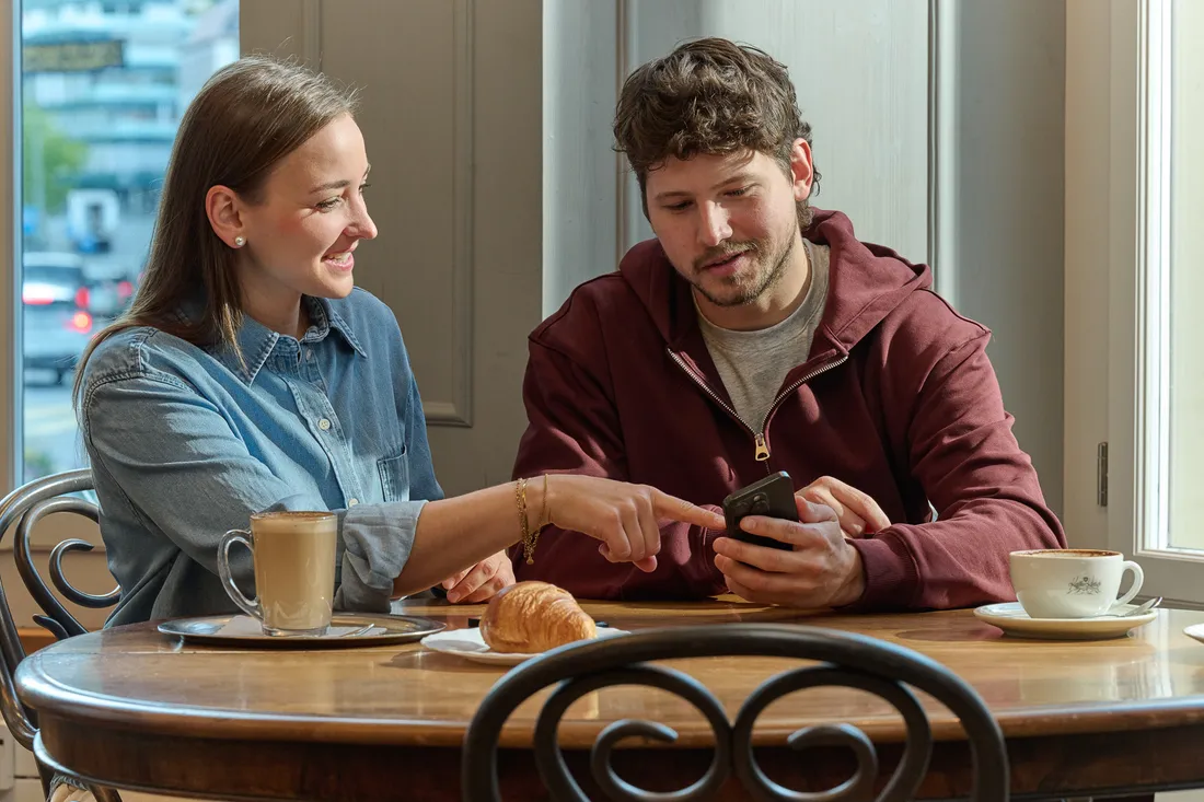 Due persone sono sedute allo stesso tavolo in un caffè e osservano insieme uno smartphone.