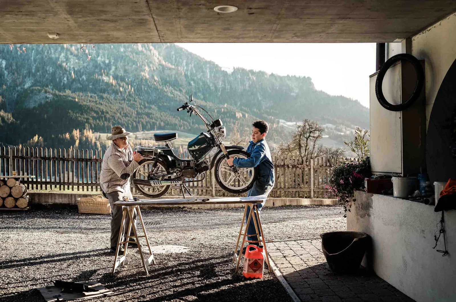 Deux personnes réparent une moto devant un paysage de montagne