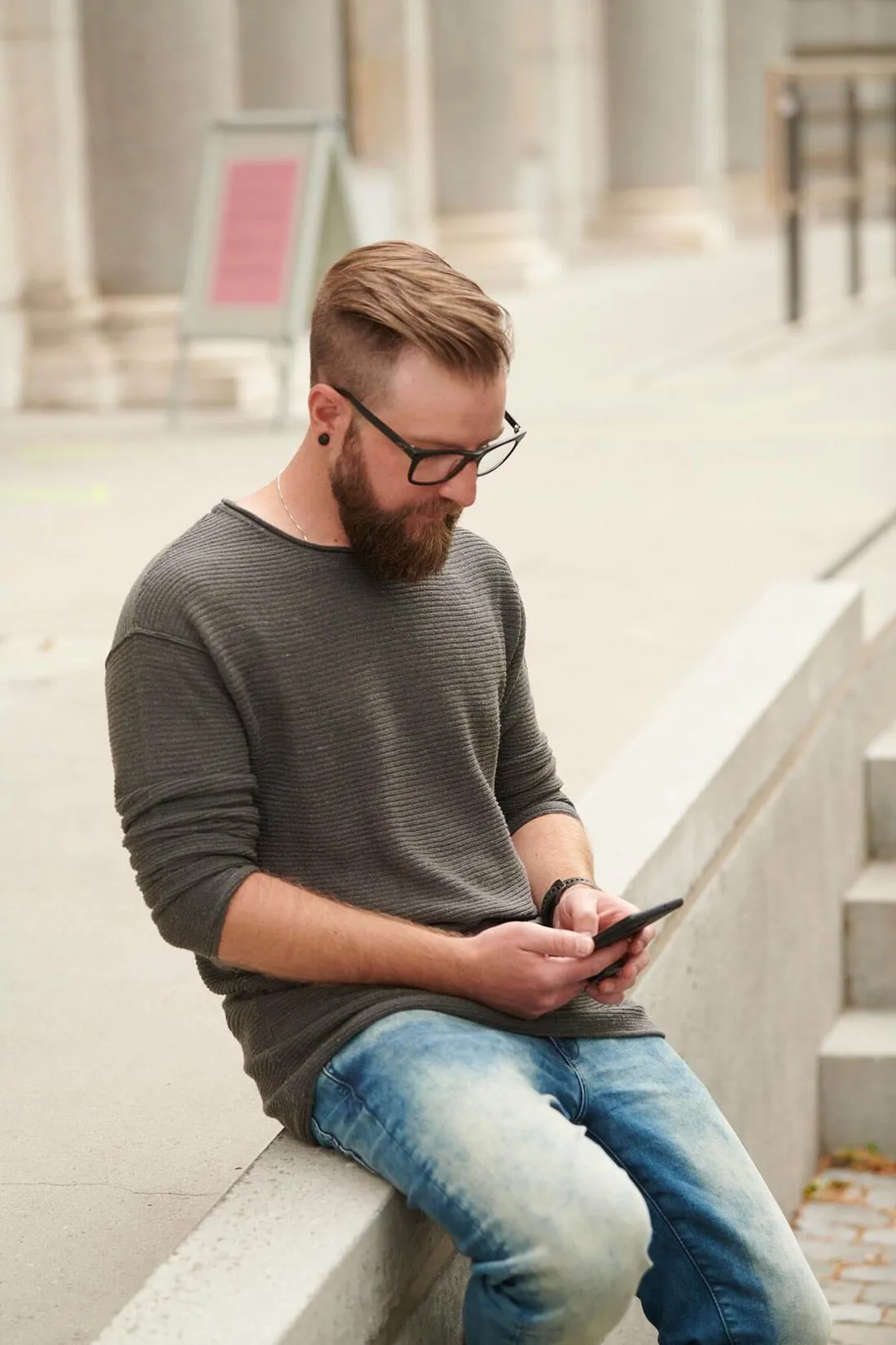 Mann sitzt auf einer Treppe und hält sein Smartphone in der Hand