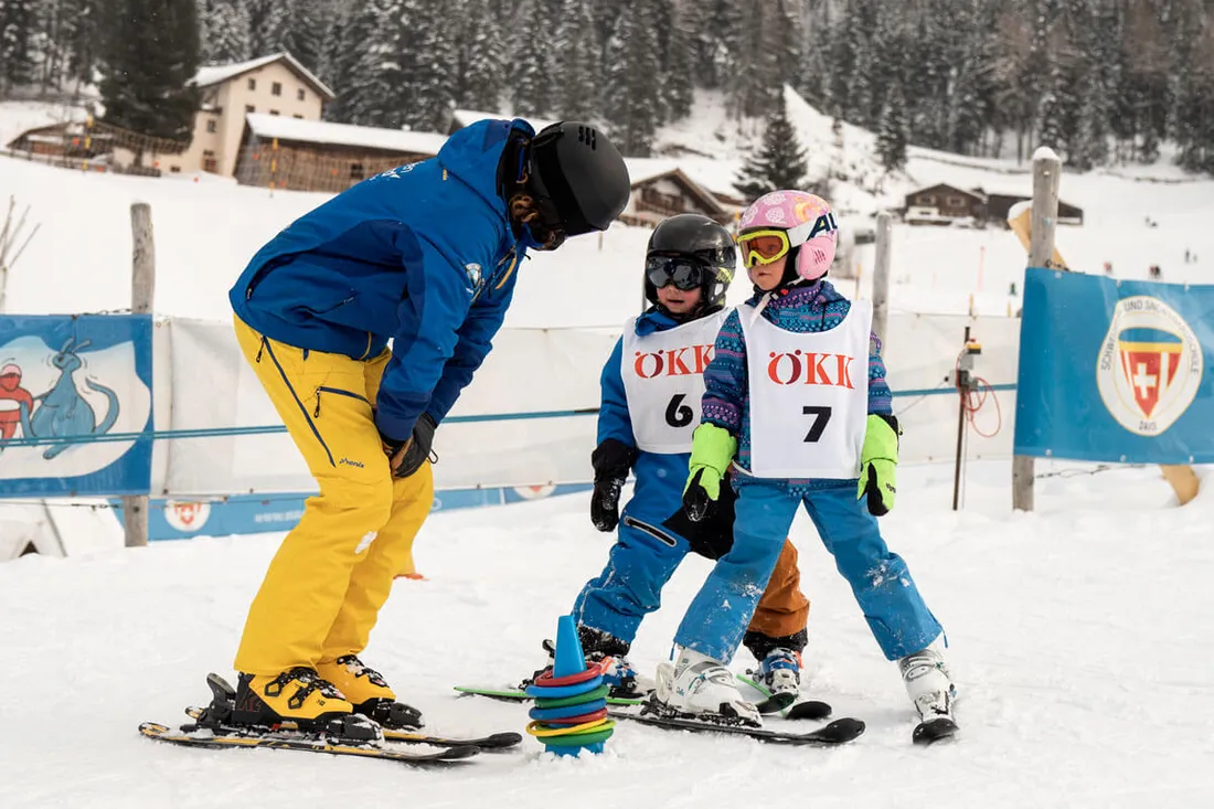 Zwei Kinder lernen mit einem Skilehrer im Schnee