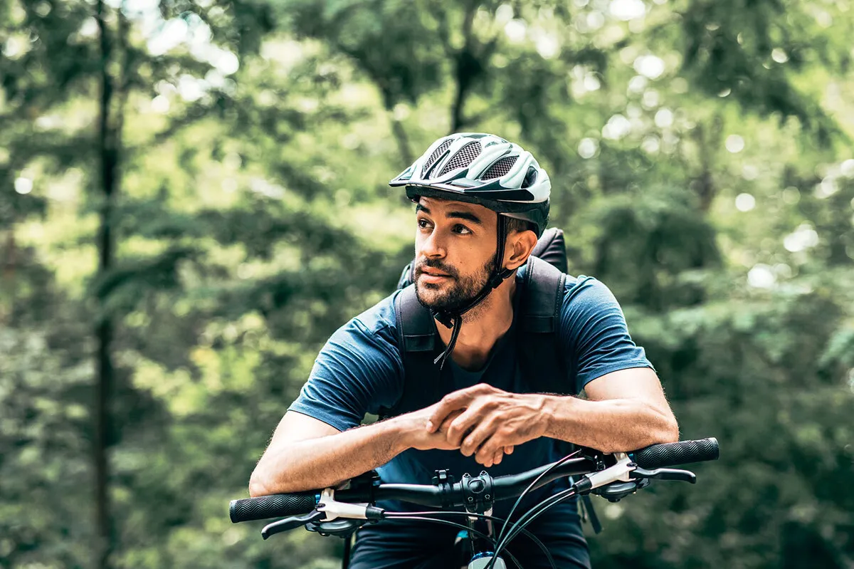 Un uomo si appoggia al manubrio della bicicletta e indossa un casco.