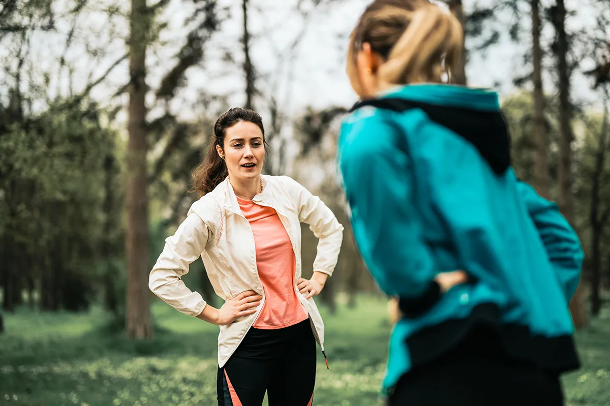 Due donne si stanno allungando dopo aver fatto jogging all’aperto nel bosco e chiacchierano tra loro.