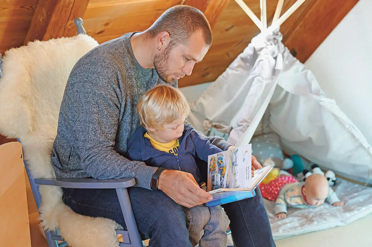 Junger Vater, der eine Geburt während Corona hatte, sieht mit seinem Kind ein Buch an