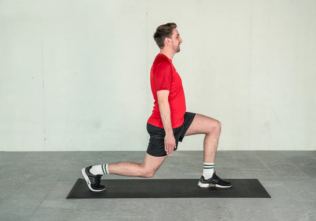 Ein junger Mann balanciert auf einer Yogamatte in einer Ausfallschritt-Position, während er sein Gleichgewicht trainiert.