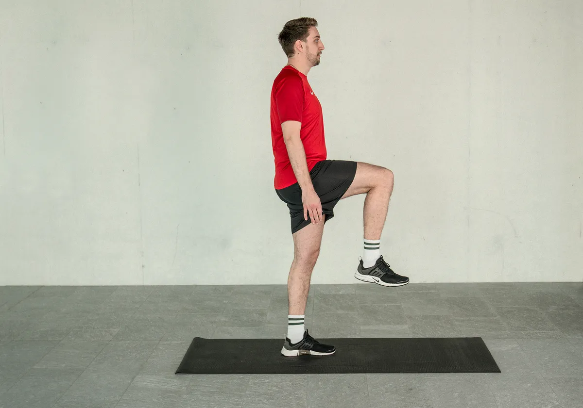 Ein junger Mann trainiert sein Gleichgewicht, während er auf einer Yogamatte steht und sich auf einem Bein im Einbeinstand befindet.