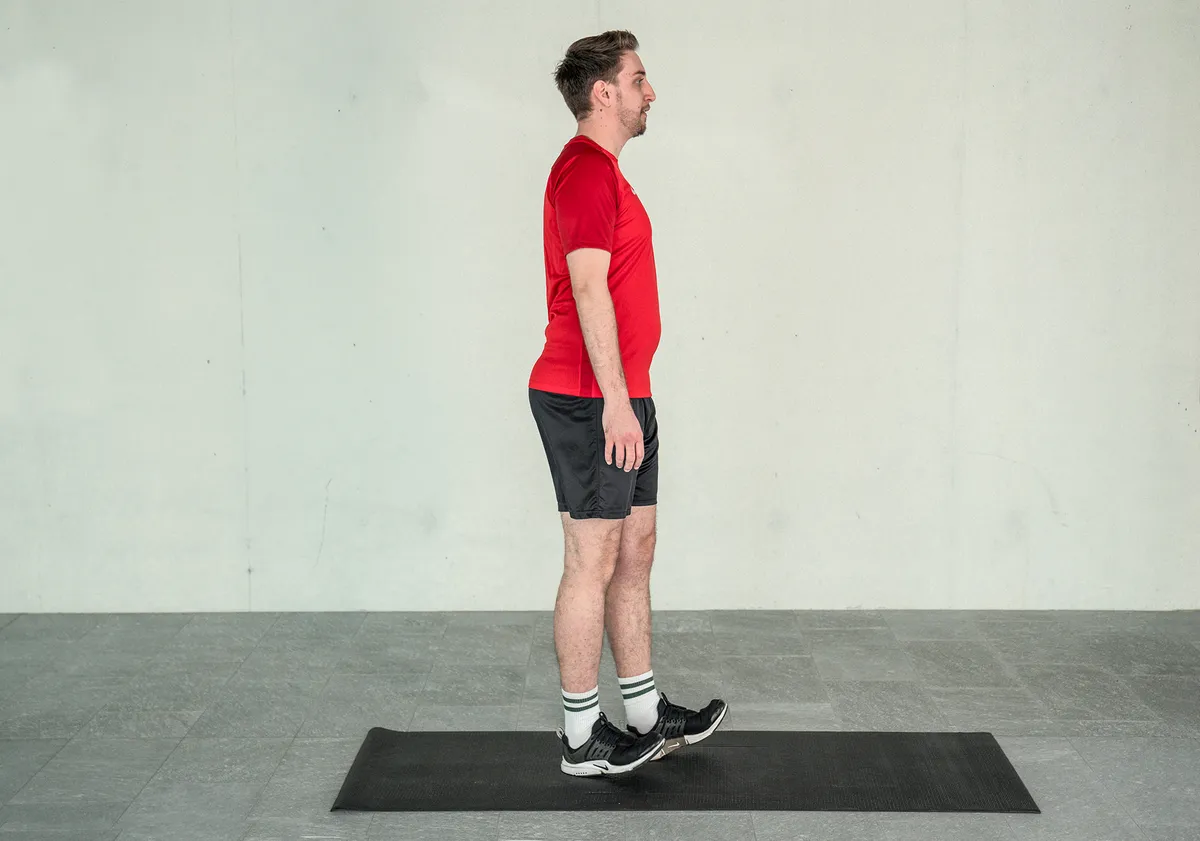 Ein junger Mann trainiert sein Gleichgewicht, indem er die Fersengang Übung auf der Yogamatte praktiziert.