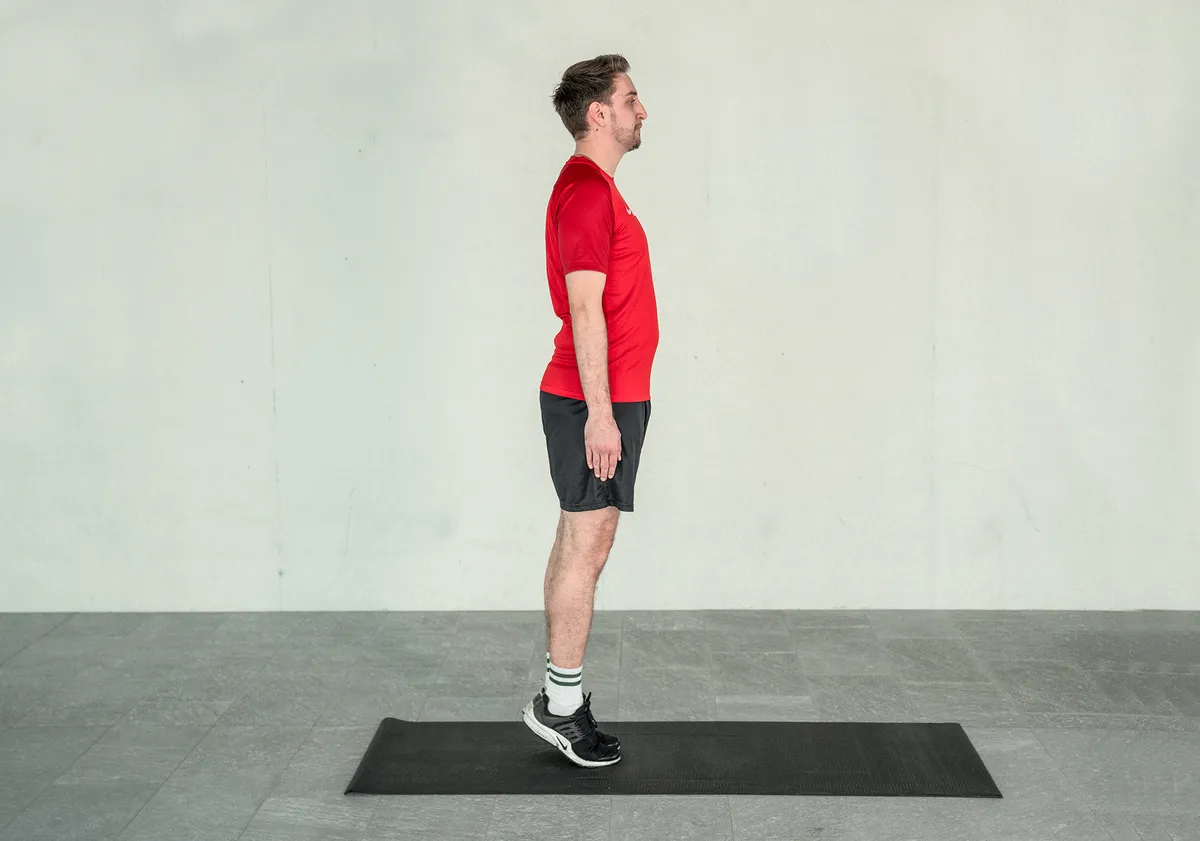 Ein junger Mann trainiert sein Gleichgewicht, indem er die Zehenstand Übung auf der Yogamatte praktiziert.