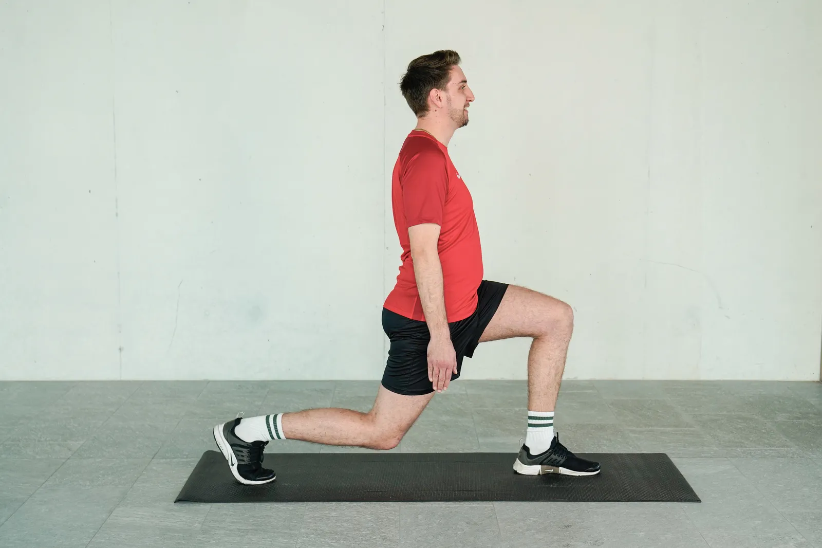 Ein junger Mann balanciert auf einer Yogamatte in einer Ausfallschritt-Position, während er sein Gleichgewicht trainiert.