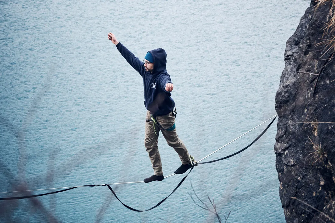 Thomas Schneebeli balanciert mit gekonnter Leichtigkeit auf der Slackline über den See, seine Arme ausgestreckt, um das Gleichgewicht zu halten.