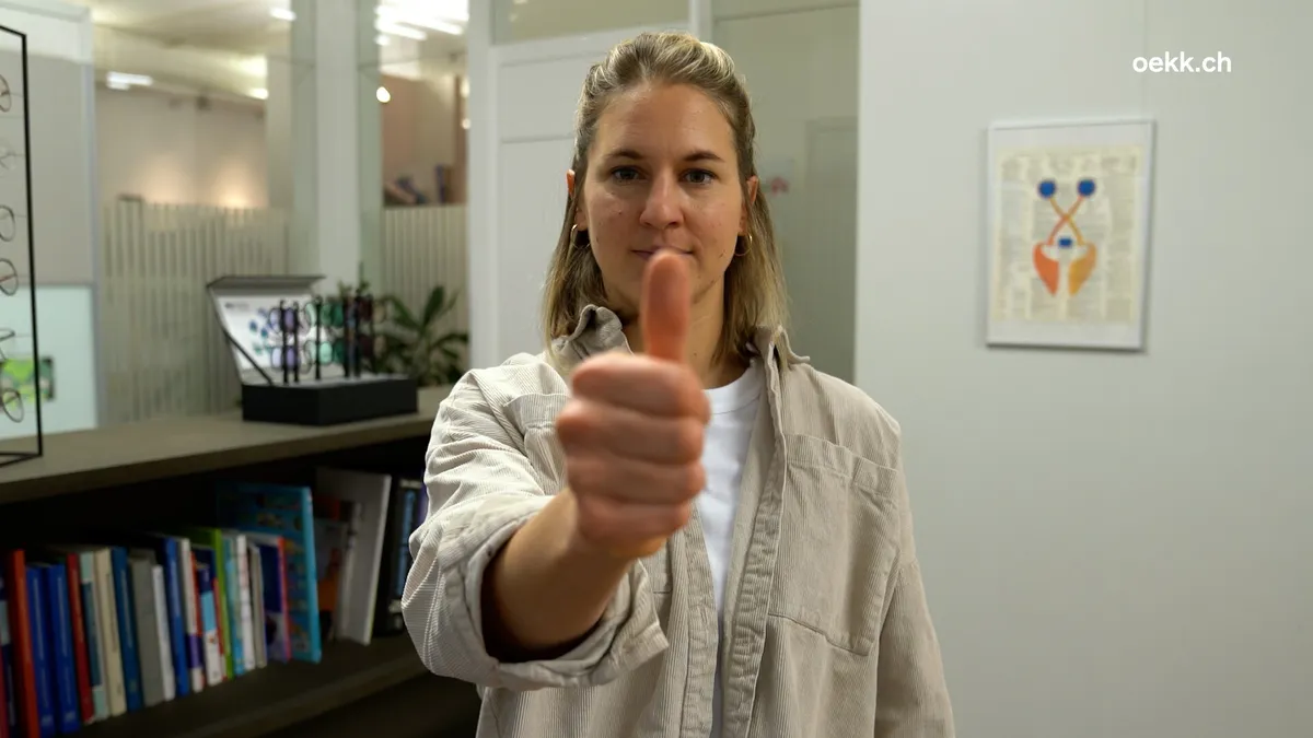 Frau führt eine Augenübung mit ihrem Daumen durch, um die Augenmuskulatur zu stärken. Im Hintergrund sind Bücherregale und ein optisches Fachgeschäft zu sehen.