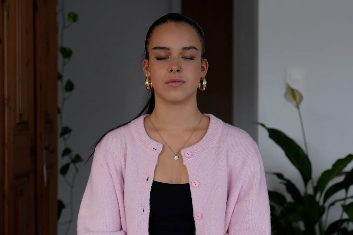 Person mit geschlossenen Augen, die entspannt sitzt und eine Atemübung zur Entspannung ausführt.