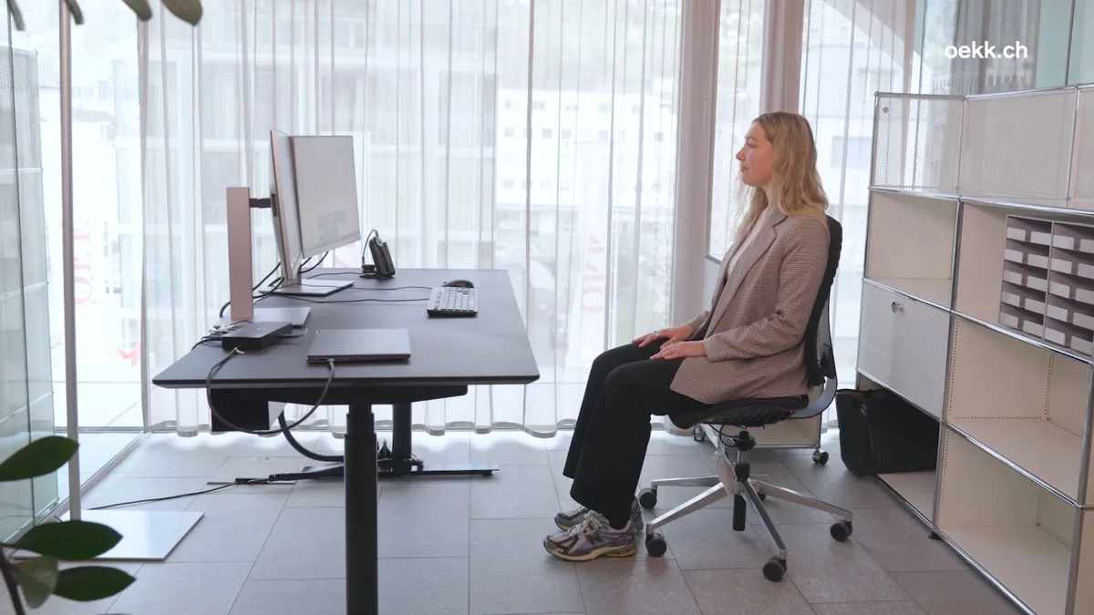 Frau sitzt auf ergonomischem Bürostuhl vor höhenverstellbarem Schreibtisch mit Computer in hellem Büro