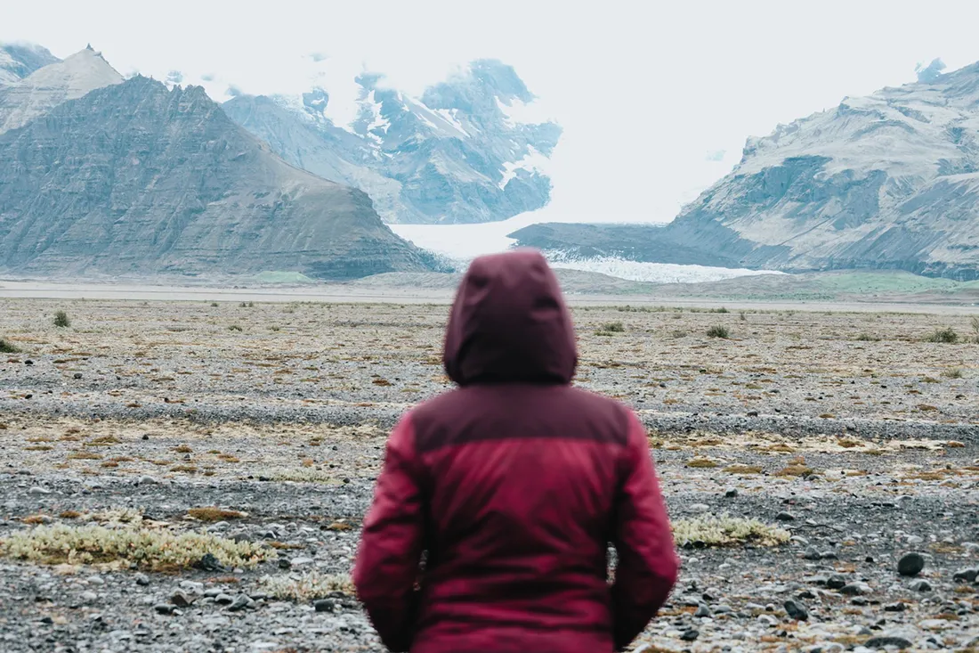 Person mit roter Jacke steht vor einer rauen Landschaft