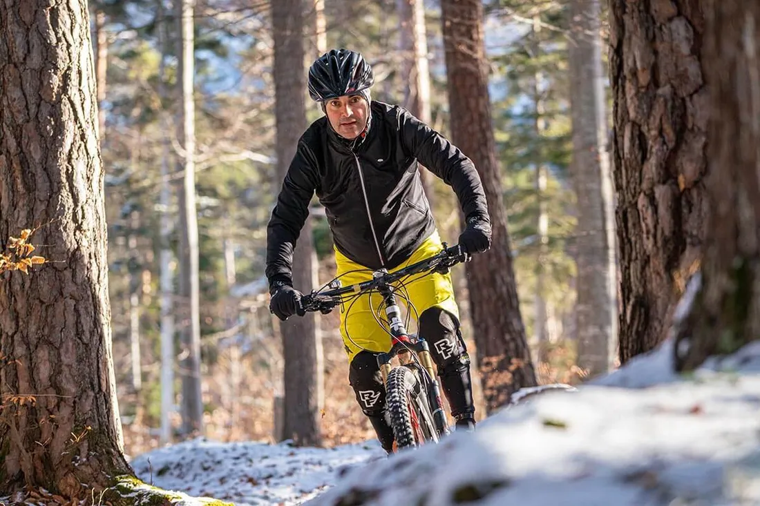 Mann fährt bei wenig Schnee mit dem Mountainbike durch den Wald