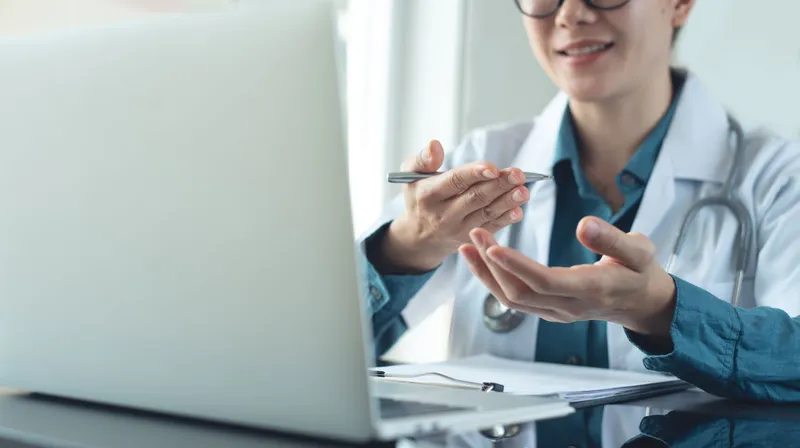 Eine medizinische Fachperson führt vor einem Laptop eine digitale Beratung durch.