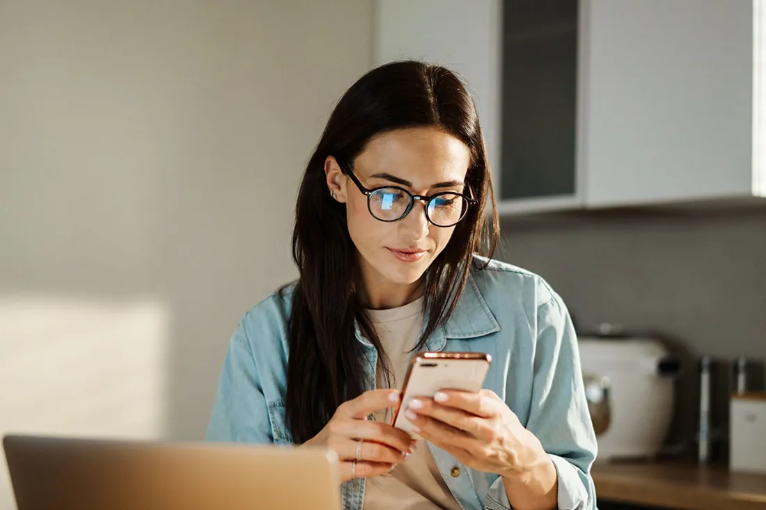 Donna seduta a un tavolo che tiene uno smartphone con entrambe le mani