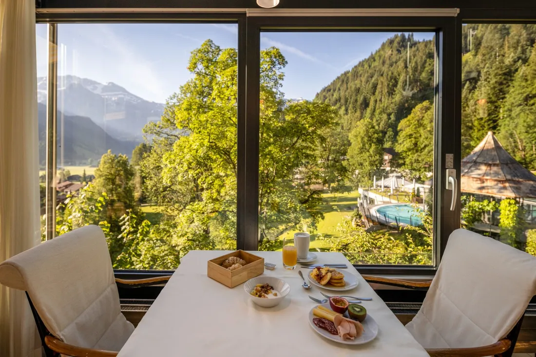 Frühstückstisch im Hotel mit Aussicht auf den Park mit Bergen