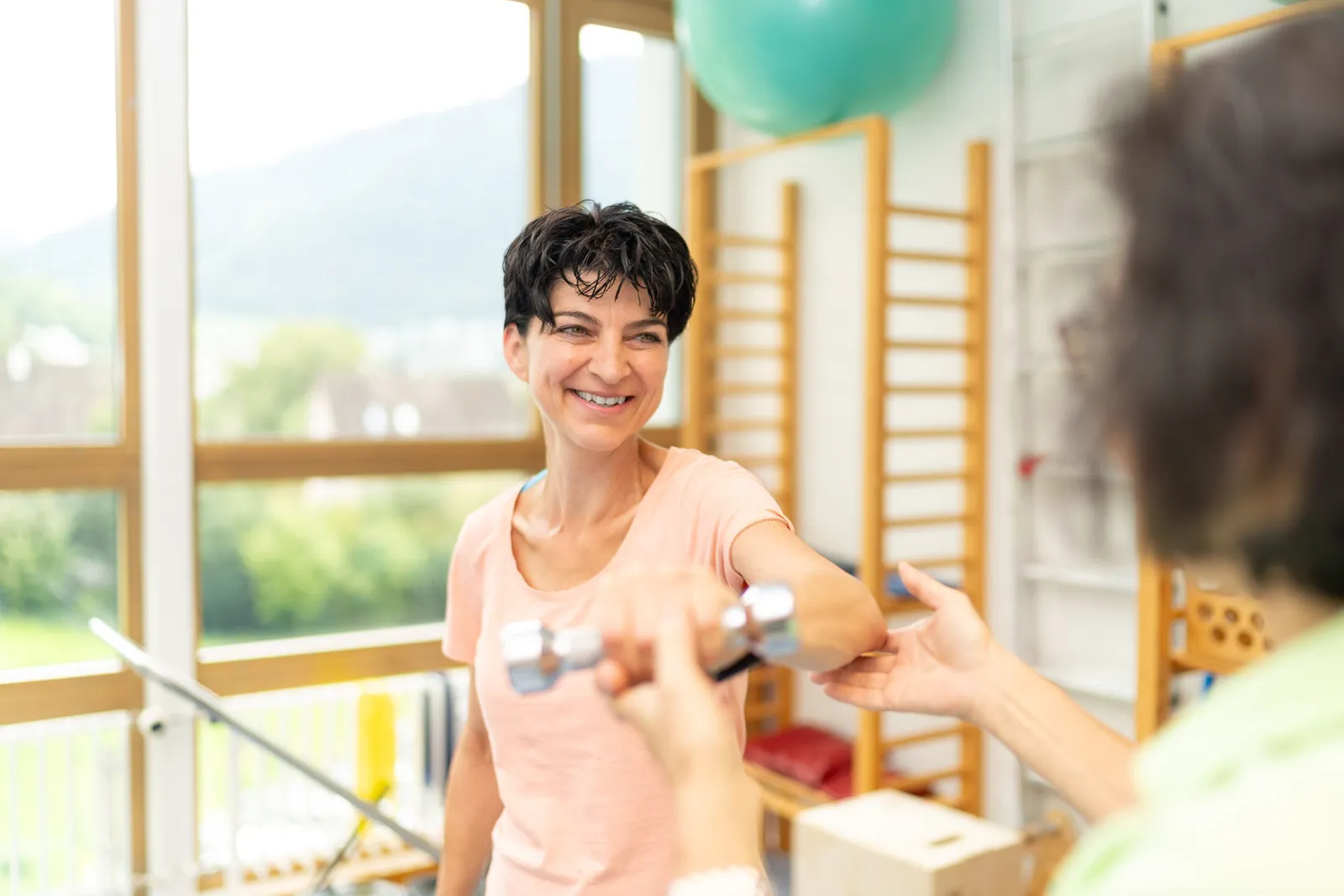 Person trainiert in einer Therapiepraxis mit einer Hantel unter fachlicher Anleitung.