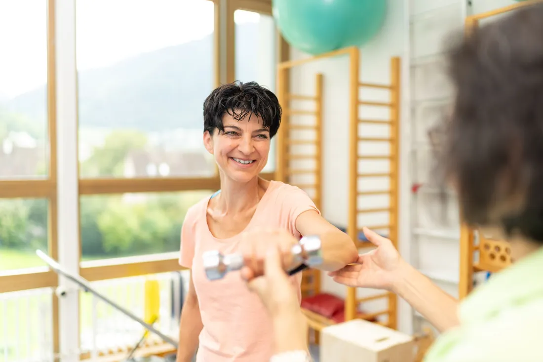 Person trainiert in einer Therapiepraxis mit einer Hantel unter fachlicher Anleitung.