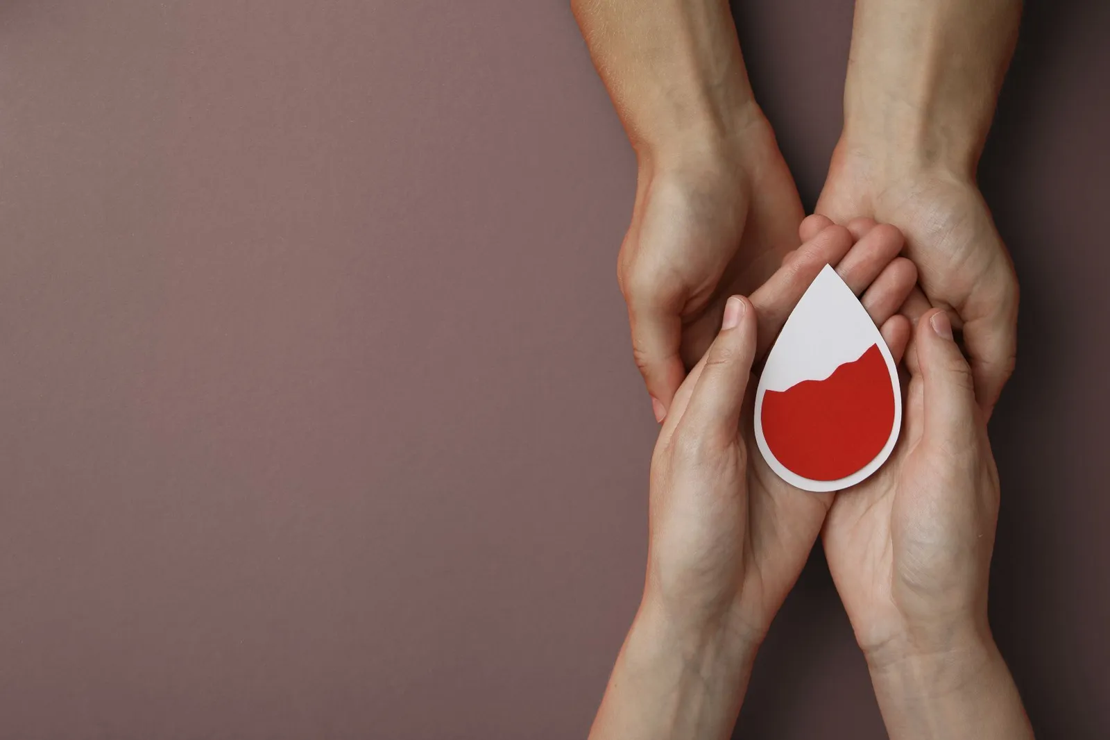 Zwei Hände halten eine weitere Hand, die eine Papierform in Tropfenform mit rotem Inhalt hält.