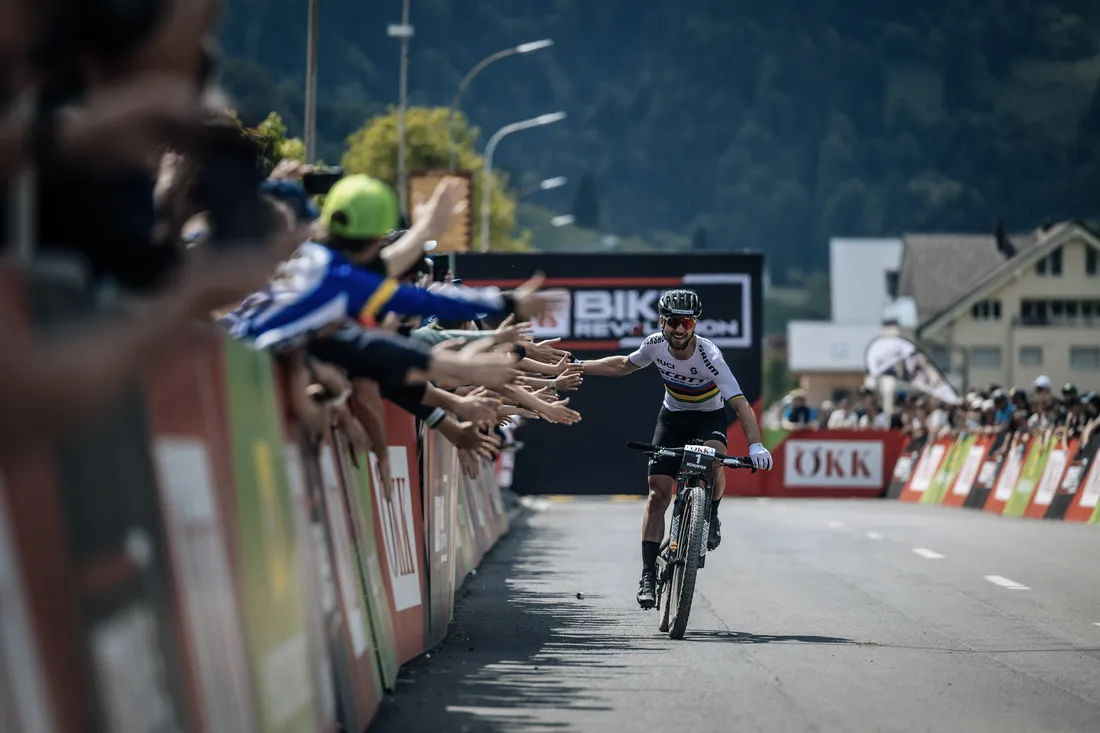 Nino Schurter überquert jubelnd die Ziellinie bei der OEKK Bike Revolution und klatscht dabei mit dem Publikum ab.