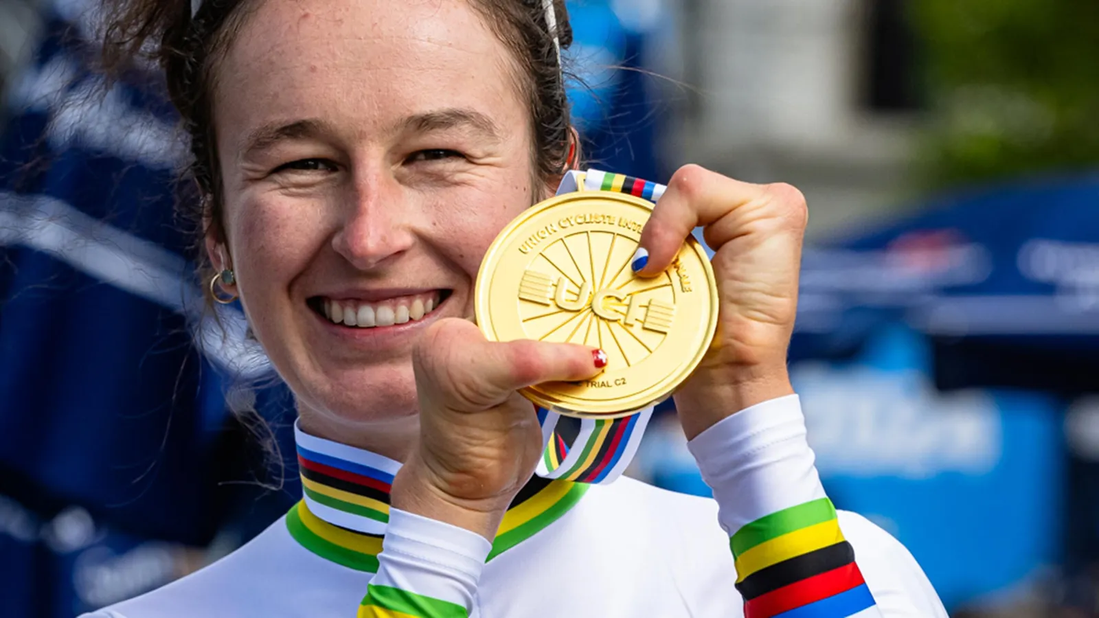 Lächende Frau hält eine Goldmedaille mit buntem Band vor ihrem Gesicht