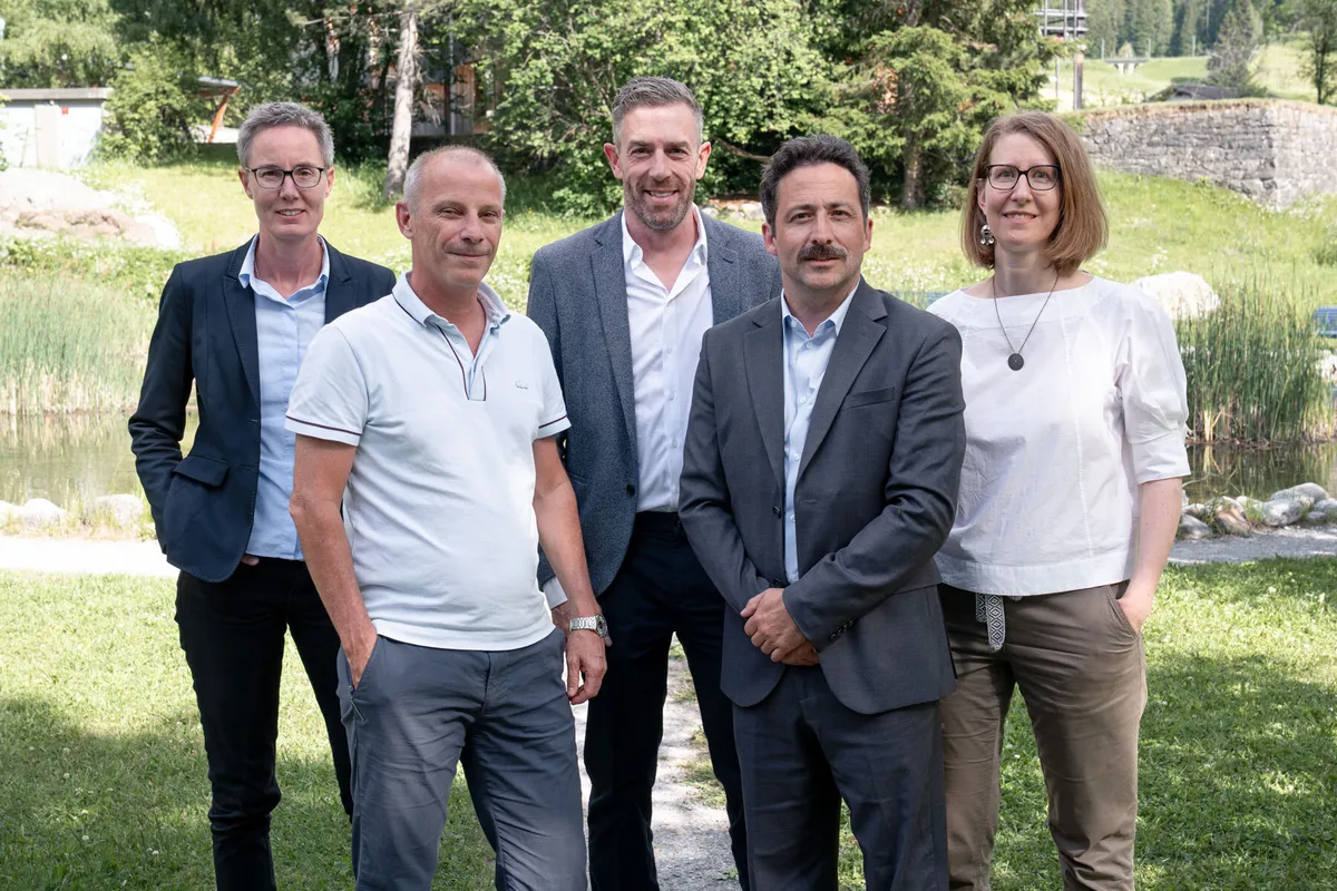 Il consiglio di amministrazione di ÖKK è riunito in un piccolo gruppo all’aperto su un prato vicino a un corso d’acqua e alberi.