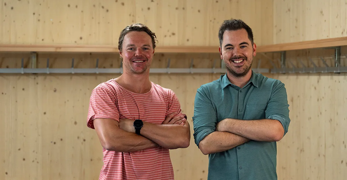 Eishockeyprofi Jan Neuenschwander (links) steht mit Moderator Fabio Nay (rechts) in einem Holzraum, beide mit verschränkten Armen und einem Lächeln im Gesicht.