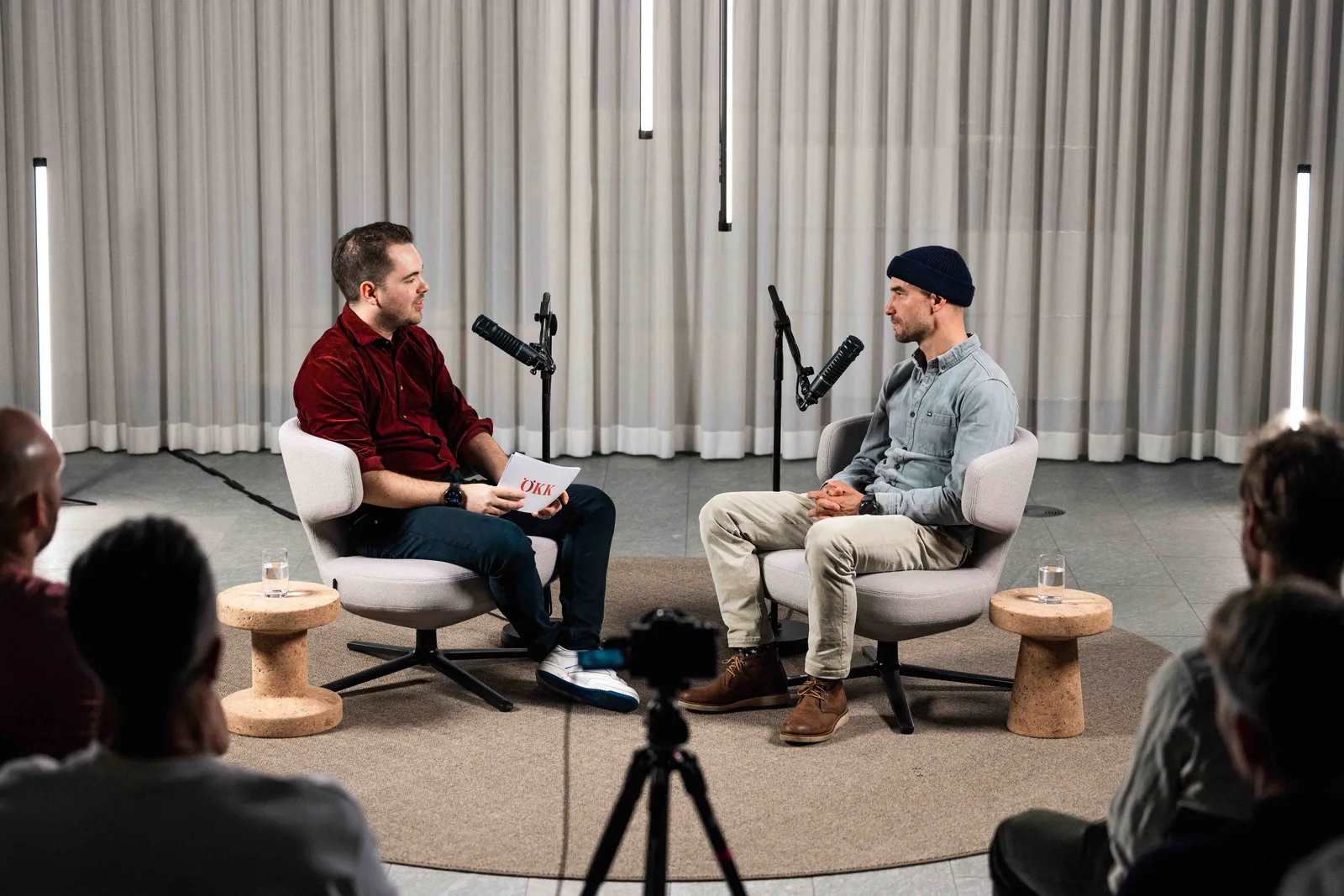 Fabio Nay und Nino Schurter sitzen sich in einem Studio gegenüber und führen ein Podcast-Gespräch mit Mikrofonen, während ein kleines Publikum zuhört.