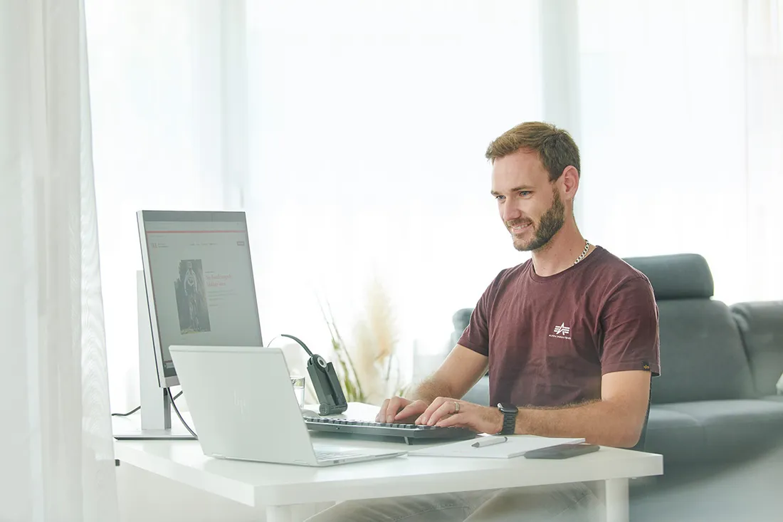 Mann sitzt an einem Schreibtisch und arbeitet an einem Laptop in einem hellen Raum