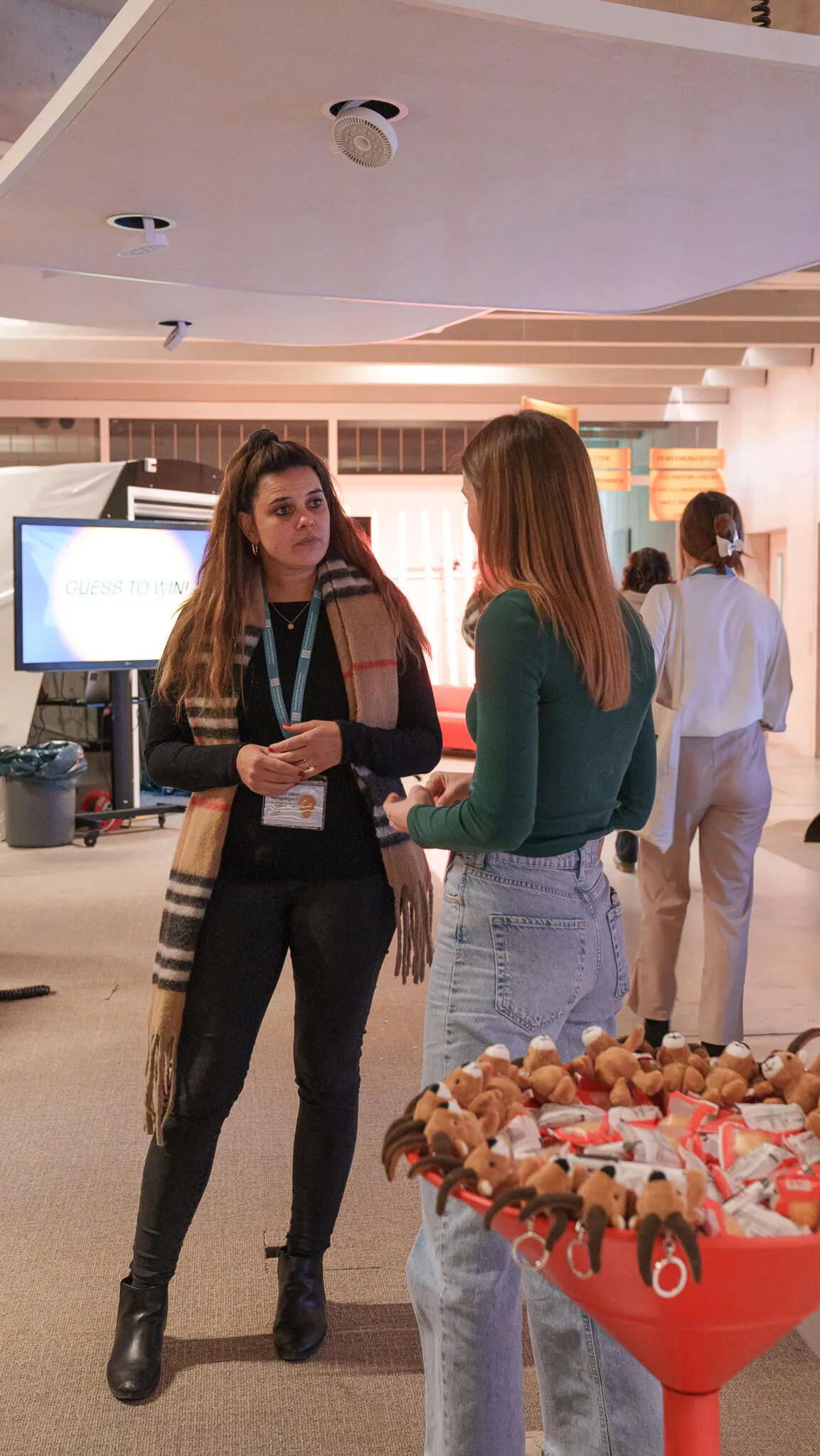 Zwei Frauen im Gespräch in einem hellen Raum mit Informationsständen, im Vordergrund ein Tisch mit vielen kleinen Stofftieren.
