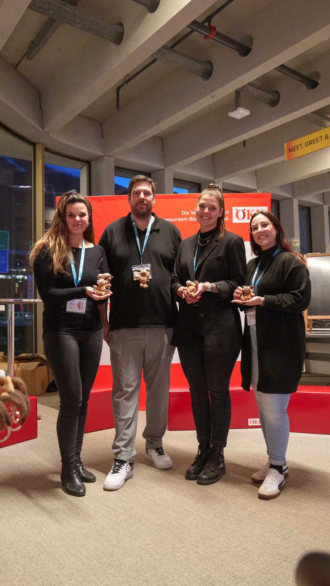 Vier Personen stehen nebeneinander, alle tragen schwarze Oberteile und halten kleine Nusstörtchen in den Händen. Im Hintergrund roter Messestand mit weißem Schriftzug.